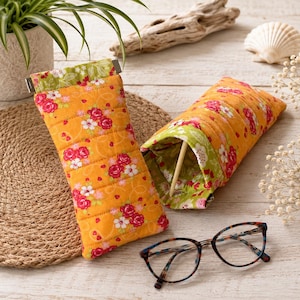 May include: Two quilted fabric cases for eyeglasses featuring a vibrant orange background with a floral pattern of red roses and white blossoms. The interior lining is a light green fabric with a white leaf print. A pair of tortoiseshell glasses.