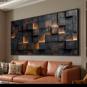 Könnte beinhalten: Große, gerahmte Wandkunst mit einem strukturierten, dunkelgrauen Design aus quadratischen Blöcken mit warmer, orangefarbener Beleuchtung. Das Kunstwerk hängt über einem braunen Ledersofa mit dekorativen Kissen.
