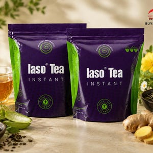 May include: Two purple Iaso Tea Instant pouches with green accents are shown, alongside a cup of tea and ingredients such as ginger and aloe vera. The packaging displays the text "Iaso Tea Instant" in white, with a green spiral design.