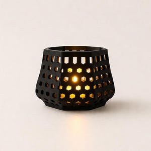 Könnte beinhalten: Ein schwarzer, geometrischer Kerzenhalter mit Wabenmuster. Der Kerzenhalter ist von innen beleuchtet und wirft einen warmen, gelben Schein durch die ausgeschnittenen Formen. Das Design ist modern und dekorativ.