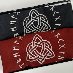 Peut inclure: Deux écharpes, une noire et une bordeaux, sont présentées dans une boîte. Chaque écharpe présente un motif de nœud celtique argenté et des runes. Les écharpes sont en tissu doux et pliées.