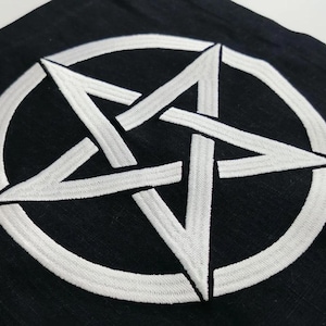 May include: A black fabric item featuring a white embroidered pentagram design. The five-pointed star is enclosed within a circular border, with the embroidery showing a distinct textured stitch pattern against the dark background material.