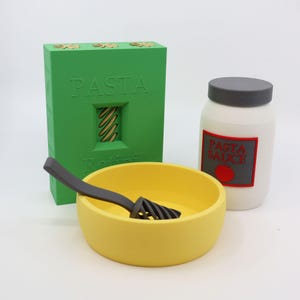 May include: A green box labeled "PASTA" with a window showing pasta, a yellow bowl with a dark gray utensil, and a white jar labeled "PASTA SAUCE" with a red label and a tomato illustration.