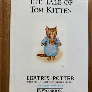 May include: A white book cover titled The Tale of Tom Kitten by Beatrix Potter. The cover features a central illustration of a brown tabby kitten wearing a blue jacket and blue trousers. The text includes The Original and Authorized Edition.