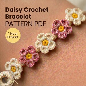 Puede incluir: Un patrón PDF de pulsera de ganchillo de margaritas. La pulsera presenta flores de margarita de ganchillo en rosa, crema y amarillo. El texto "1 Hour Project" está en un círculo amarillo. Se ve un ovillo de hilo.