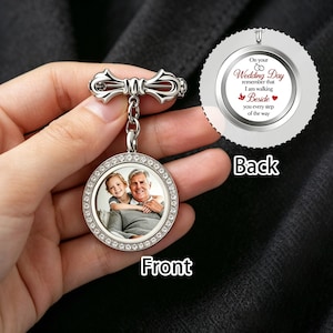 Puede incluir: Un broche de boda plateado con un colgante redondo. La parte delantera del colgante presenta una foto de un niño sonriente y un hombre mayor, rodeados de cristales transparentes. La parte trasera del colgante tiene el texto "On your Wedding Day...Beside you every step of the way."