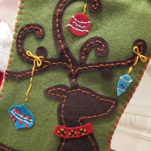 May include: A green felt Christmas stocking with a brown felt reindeer applique. The reindeer has a red and black collar and is decorated with colorful ornaments.