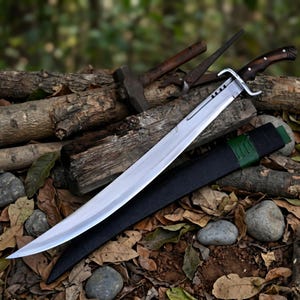 May include: A large, curved sword with a polished silver blade and a dark wooden handle. The sword rests on a bed of logs and leaves, with a black sheath and green accents. A hammer and other tools are in the background.