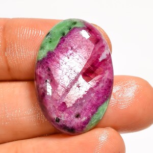Op de afbeelding: Een ovaalvormige cabochon edelsteen met een levendig magenta-roze centrum met zichtbare kristallijne insluitingen en donkergroene minerale secties langs de randen. Het gepolijste oppervlak reflecteert het licht en benadrukt het kleurcontrast.