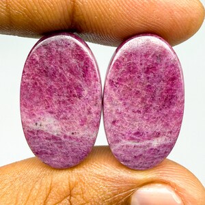 May include: Two oval-shaped cabochons with a polished surface, featuring a deep magenta and pink color palette with natural crystalline inclusions and white veining throughout the stones, displaying a smooth, rounded, and symmetrical gemstone form.