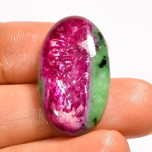 Può includere: Una gemma cabochon di forma ovale caratterizzata da un centro rosa magenta vibrante con una consistenza cristallina, delimitata da una sezione verde chiaro opaca e liscia contenente piccole inclusioni minerali nere, lucidata con una finitura brillante.