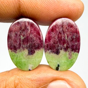 May include: Two oval-shaped cabochons featuring a distinct color split. The upper portion of each stone is a deep, translucent magenta-red with visible internal crystalline fractures, while the lower section is an opaque, solid light lime green.