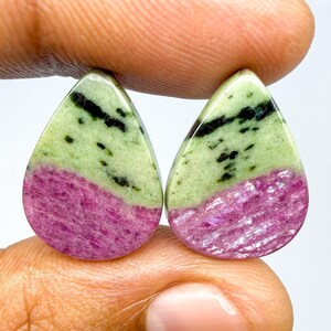 May include: Two teardrop-shaped cabochons featuring a distinct color split. The upper portion is a pale mint green with dark black inclusions, while the lower section is a vibrant, textured magenta pink. Both stones have a smooth, polished finish.