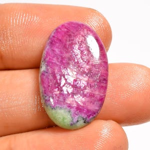 Peut inclure: Une pierre précieuse cabochon de forme ovale présentant un centre rose magenta vif avec une base vert clair distincte. La surface de la pierre présente une texture polie et brillante avec des inclusions cristallines naturelles visibles.