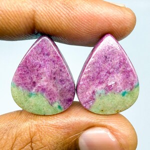 May include: Two pear-shaped cabochons featuring a distinct color split. The upper portion of each stone is a vibrant magenta-pink with crystalline texture, while the lower section is a solid, opaque light green with small teal inclusions.