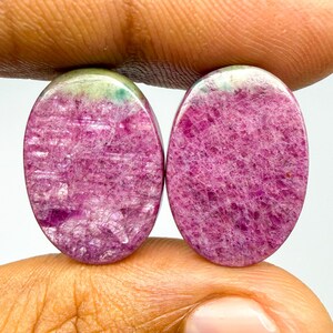 May include: Two oval-shaped cabochon gemstones featuring a vibrant magenta and deep pink crystalline texture with subtle hints of pale green at the top edges. These polished stones display a natural, multifaceted internal structure throughout.