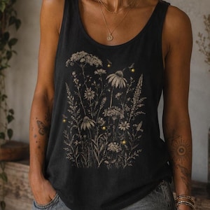 May include: A black sleeveless tank top featuring a detailed botanical print of various wildflowers and grasses in a muted beige tone, accented with small, glowing yellow firefly-like dots scattered throughout the floral illustration.