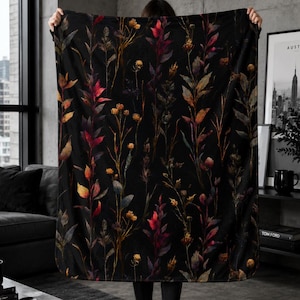 May include: A rectangular throw blanket featuring a dark black background with a repeating botanical pattern of tall, slender wildflowers and foliage in shades of deep red, burnt orange, muted yellow, and dark green, with rounded corners.