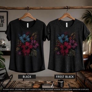 Puede incluir: Dos camisetas, una negra y otra negra helada, cada una con un dise&ntilde;o floral con flores rojas, azules y moradas. Las camisetas cuelgan de perchas de madera. El fondo incluye el texto "BORN TO BE WILD".