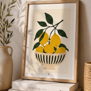 Könnte beinhalten: Ein gerahmter Kunstdruck mit einer grafischen Illustration einer Schale voller gelber Zitronen und dunkelgrüner Blätter. Die Schale ist cremefarben mit vertikalen dunkelgrünen Streifen. Die Zahl 2 ist unten in der Mitte des Drucks abgebildet.