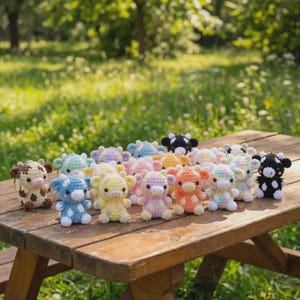 May include: A collection of colorful, crocheted cow figurines in various colors, including brown, blue, yellow, pink, orange, and black. The cows are arranged on a wooden picnic table, with a blurred green background of grass and trees.