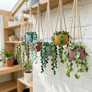 May include: A collection of handmade crochet hanging planters in various colors, including green, blue, orange, yellow, and pink. Each planter is suspended by a natural rope and filled with trailing green crochet vines, creating a charming, handcrafted display.