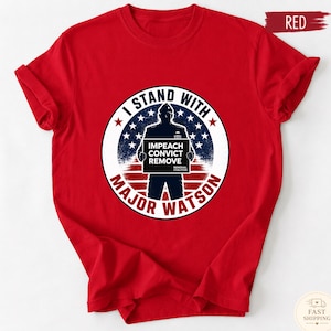 May include: A red short-sleeved t-shirt featuring a circular graphic with a silhouette of a person holding a sign that reads IMPEACH CONVICT REMOVE. The graphic includes a blue background with white stars and red stripes, and the text I STAND WITH MAJOR WATSON.
