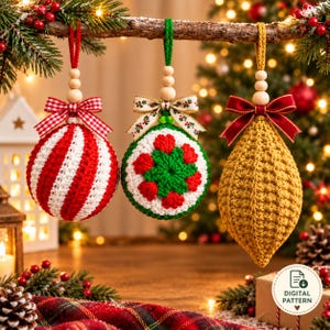 Op de afbeelding: Drie gehaakte kerstornamenten hangen aan een tak. De eerste is een rood-wit gestreepte bol met een rode gingham strik. De tweede is een witte bol met een groen en rood bloemmotief en een strik met patroon. De derde is een gouden druppelvorm met een donkerrode fluwelen strik.