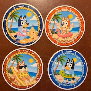 Könnte beinhalten: Vier runde Untersetzer mit Zeichentrick-Hundefiguren in Strandmotiven. Jeder Untersetzer hat einen Rand in Seiloptik. Die Designs zeigen Figuren beim Bau von Sandburgen, mit einem pinken Flamingo-Schwimmring, beim Entspannen auf einer Liege und mit einem grünen Schwimmring.