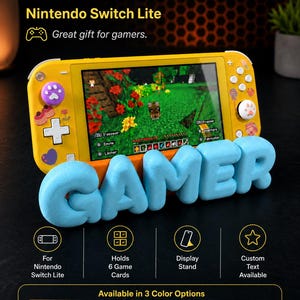 Può includere: Una console Nintendo Switch Lite gialla appoggiata su un supporto azzurro stampato in 3D a forma della parola GAMER. Lo schermo mostra un videogioco a blocchi. Il supporto ha fessure per sei schede di gioco ed è presentato con del testo.