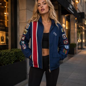 May include: A navy blue zip-up jacket featuring a prominent vertical red stripe bordered by white on the right side, multiple colorful embroidered patches on both sleeves, and the white cursive text LDR embroidered on the upper left chest area.