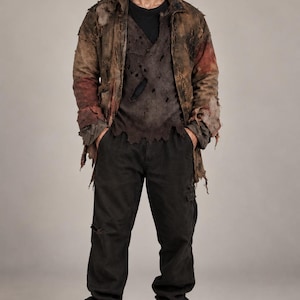 May include: A distressed brown jacket with frayed edges and patches of red, worn over a dark gray t-shirt with multiple small holes. The outfit includes black cargo pants with a visible tear on the right leg and dark brown lace-up boots.