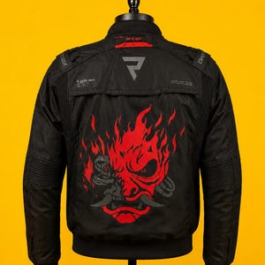 May include: A black jacket featuring a large red graphic of a stylized robotic samurai mask on the back. The jacket includes a small grey triangular logo at the top, red text reading "Ride Of Spirit" on the collar, and ribbed detailing on the shoulders.