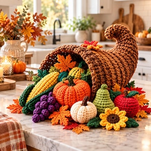 May include: A brown crocheted cornucopia overflowing with various crocheted items including a yellow corn cob, a bright orange pumpkin, a white pumpkin, a green pear, a red apple, purple grapes, a yellow sunflower, and several orange maple leaves.