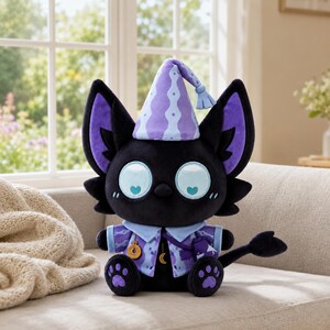 May include: A black plush cat toy wearing a light purple pointed hat with a tassel, a light blue collared shirt with a patterned design, and a small satchel. The cat has large light blue eyes with heart-shaped pupils and purple paw pads.