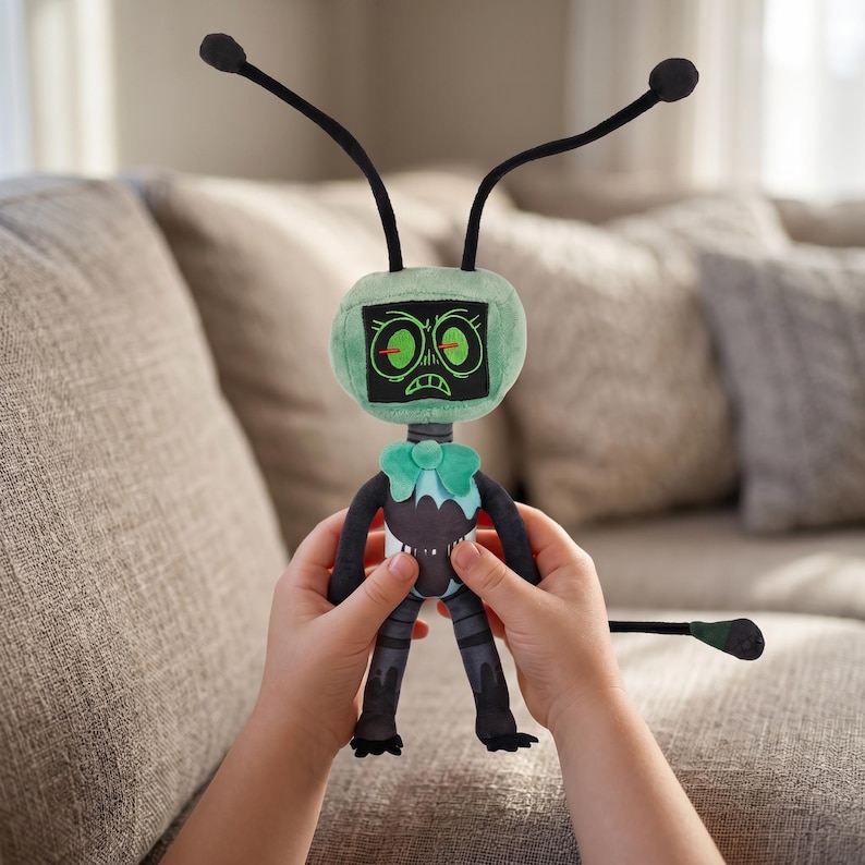 May include: A plush toy robot with a green head and a black body. The robot has two black antennae and a green bow tie. The robot's face has two glowing green eyes and a frowning mouth. The robot is being held by a person.