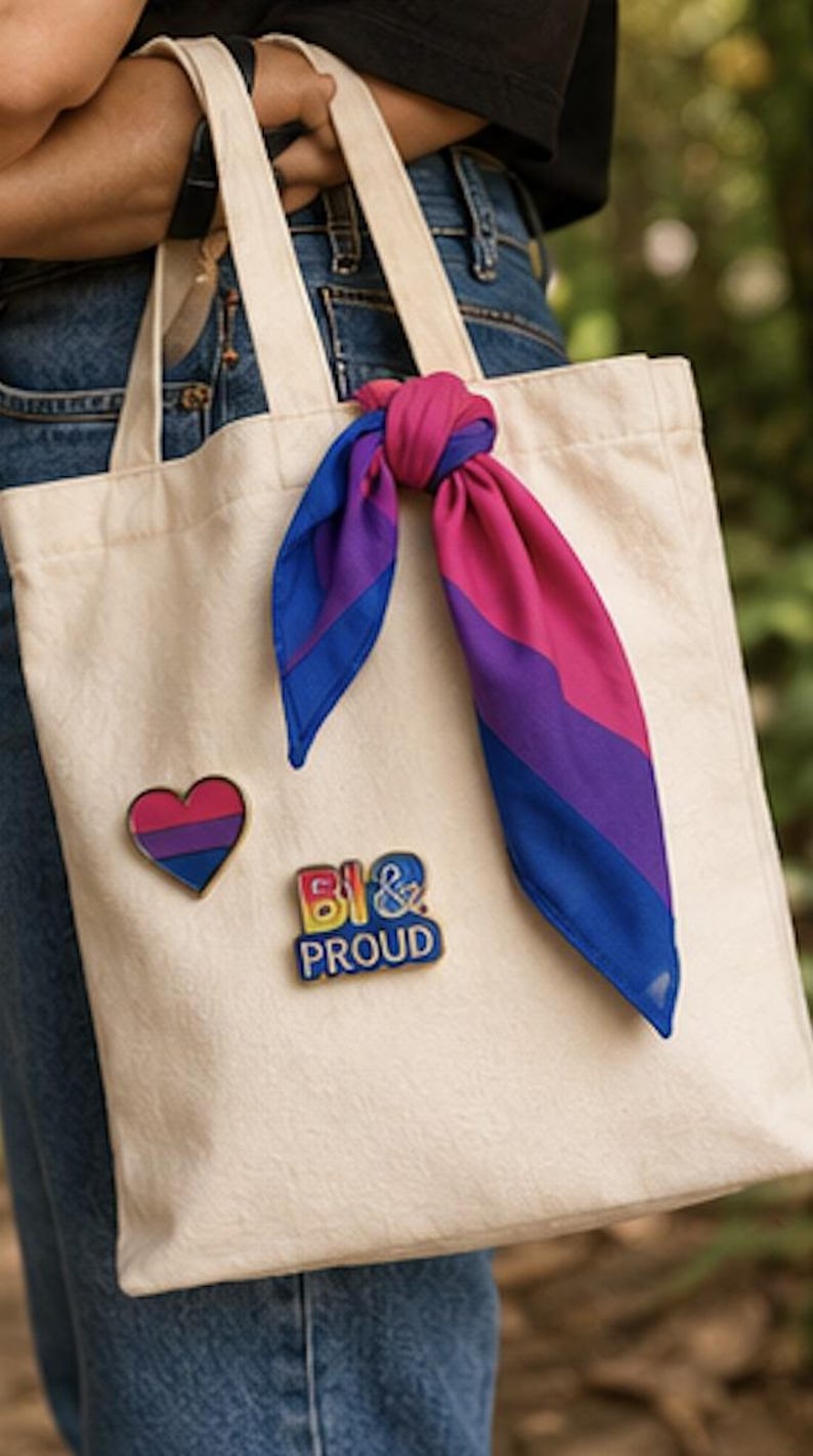 May include: A cream-colored tote bag with a heart-shaped pin and a pin that says "BI & PROUD". A scarf tied to the handle displays the bisexual pride flag colors: pink, purple, and blue. The bag is carried by a person wearing blue jeans.