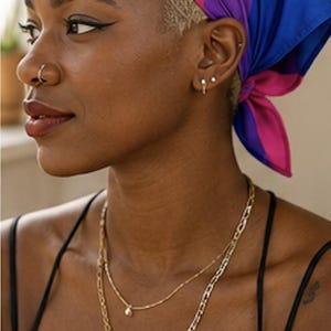 May include: A person wearing a headscarf in the colors of the bisexual pride flag: pink, purple, and blue. The person is also wearing two gold necklaces and a black tank top. The person has a nose ring and earrings.