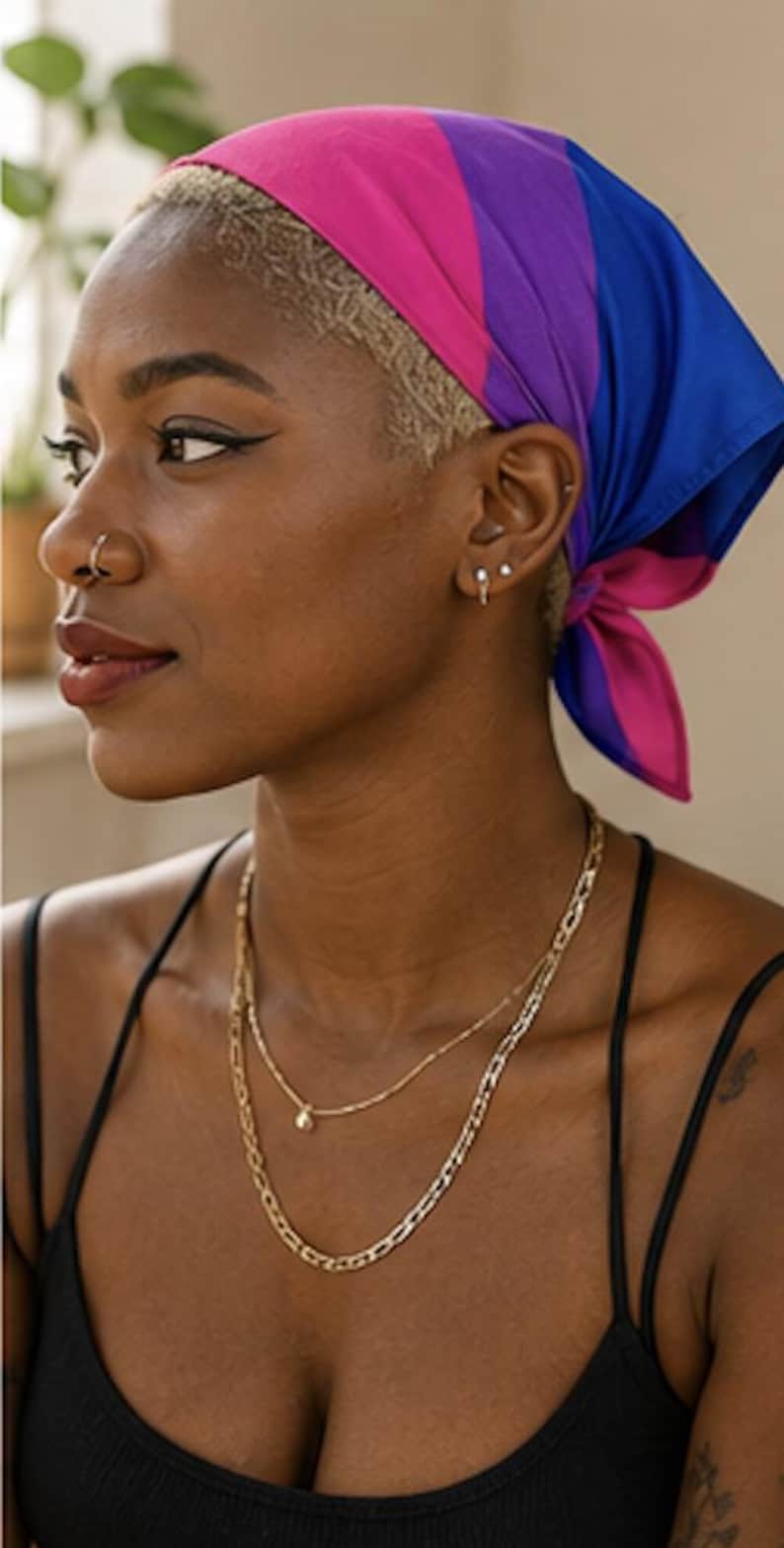May include: A person wearing a headscarf in the colors of the bisexual pride flag: pink, purple, and blue. The person is also wearing two gold necklaces and a black tank top. The person has a nose ring and earrings.