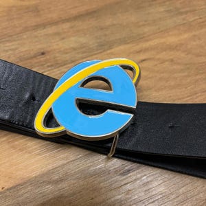 Könnte beinhalten: Ein schwarzer Ledergürtel mit einer silbernen Schnalle, die das blaue und gelbe Logo des Internet Explorers zeigt. Die Schnalle ist leuchtend blau mit einem gelben Orbit-Design.