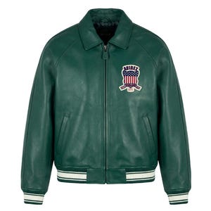 May include: A dark green leather jacket with a collared neckline and a zipper closure. The jacket features a patch on the chest with a patriotic design and white and black striped cuffs and hem. A classic bomber style.