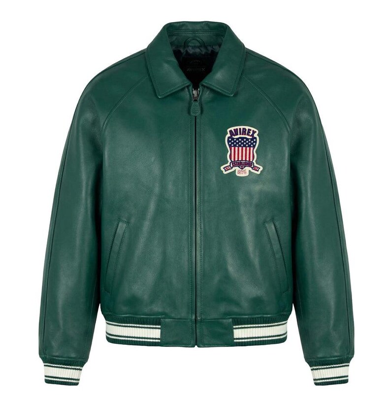 May include: A dark green leather jacket with a collared neckline and a zipper closure. The jacket features a patch on the chest with a patriotic design and white and black striped cuffs and hem. A classic bomber style.