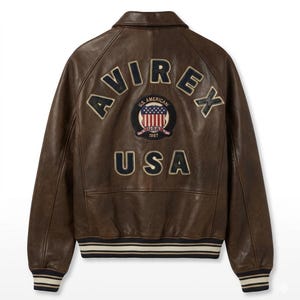 Op de afbeelding: Een bruine leren jas met het woord "AVIREX" over de bovenrug. Daaronder een patch met de woorden "U.S. AMERICAN" en "USA 1987" rond een afbeelding van de Amerikaanse vlag. Het woord "USA" staat eronder.