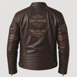May include: A dark brown leather jacket featuring quilted shoulder and lower back panels. The back displays a large Harley-Davidson logo with wings, while the sleeves include circular patches and an American flag graphic with the text H-D.