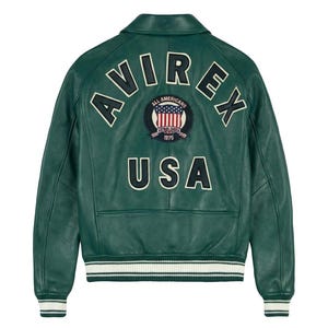 May include: A green leather jacket with the word "AVIREX" arched across the shoulders and "USA" below a circular patch. The patch features a US flag design and the words "ALL AMERICANS" and "ESTABLISHED 1975". The jacket has a white and green striped hem.