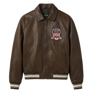 Op de afbeelding: Bruine leren jas met ritssluiting en kraag. Op de borst een patch met een rood, wit en blauw ontwerp. De jas heeft wit en zwart gestreepte manchetten en tailleband.
