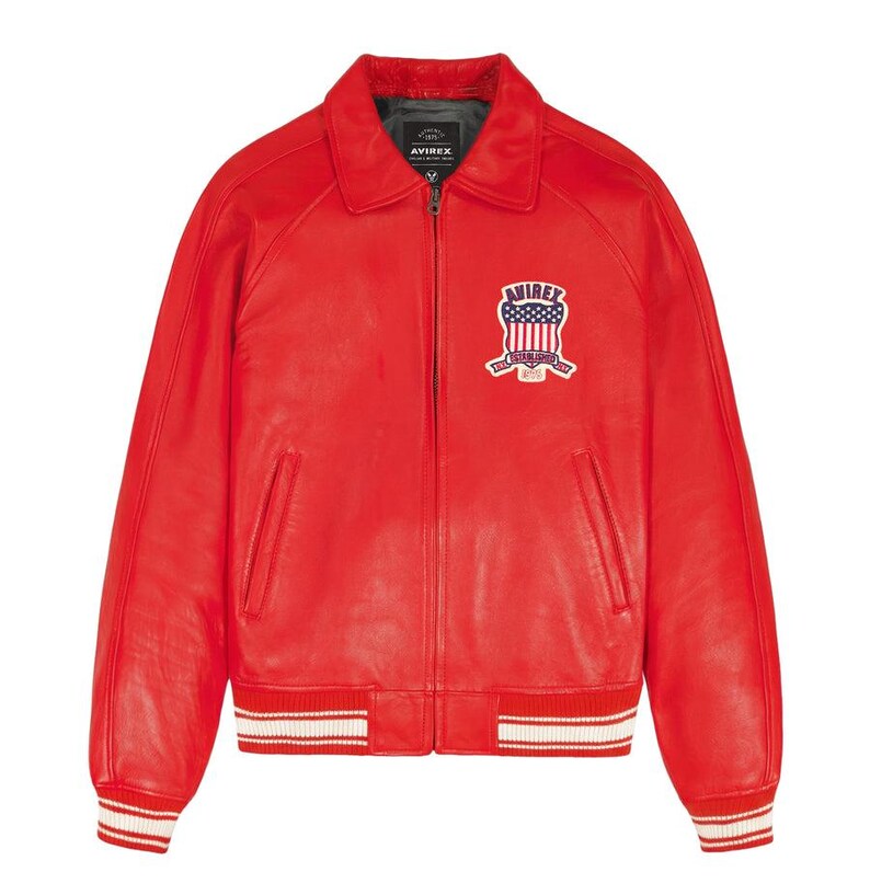 Peut inclure: Veste en cuir rouge vif de style bomber. Col chemise, fermeture &eacute;clair et poignets et ourlet c&ocirc;tel&eacute;s &agrave; rayures blanches. Un &eacute;cusson brod&eacute; avec un motif de drapeau am&eacute;ricain est cousu sur la poitrine.