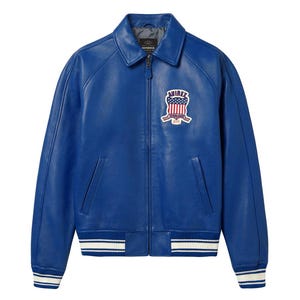 May include: A bright blue leather jacket with a zip closure, a collar, and a patch on the chest. The jacket has white and blue striped cuffs and hem. The patch features a design with stars and stripes.