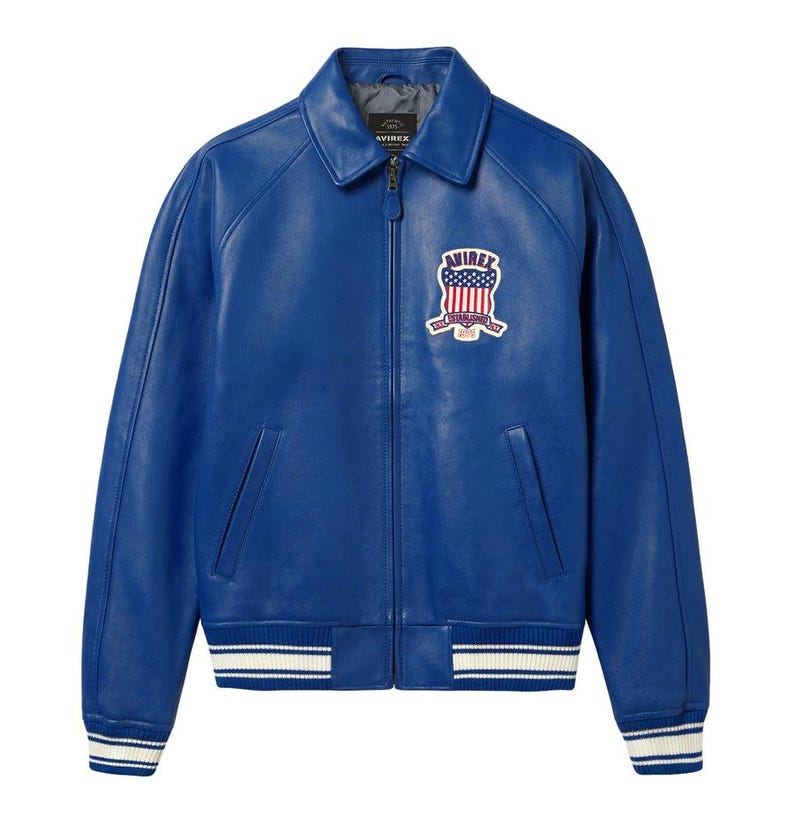 May include: A bright blue leather jacket with a zip closure, a collar, and a patch on the chest. The jacket has white and blue striped cuffs and hem. The patch features a design with stars and stripes.