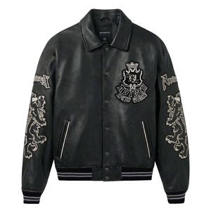 K&ouml;nnte beinhalten: Schwarze Leder-Collegejacke mit wei&szlig;en Akzenten. Mit gestickten L&ouml;wen und Textdetails auf den &Auml;rmeln und der Brust. Die Jacke hat einen Kragen, eine Knopfleiste und gerippte B&uuml;ndchen und Saum. Der Markenname "AVIREX NEW YORK" ist sichtbar.